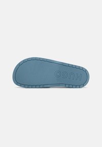 Sole di scarpa in gomma blu con texture rigata, marchio HUGO e modelli di trazione robusti per una presa migliorata.