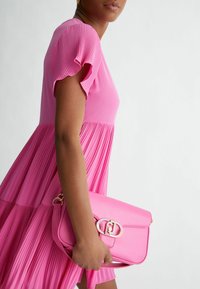 Vestido rosa con mangas cortas plisadas y falda acampanada, combinado con un bolso de cuero rosa que presenta un cierre en tono dorado.