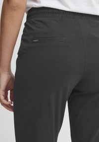 Svarte stretchbukser med elastisk midje, med en liten baklomme og en glatt, myk tekstur. Standard passform.