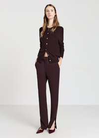 Cardigan bordeaux con bottoni dorati abbinato a pantaloni a vita alta con spacco laterale, completato da tacchi bordeaux lucidi.