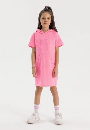 Rosa kortärmad hoodieklänning med en framficka och präglad design med "NYC". Kombineras med vita sneakers och randiga strumpor.
