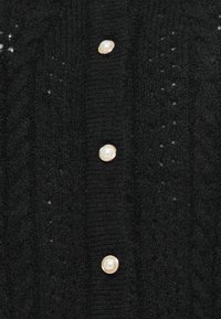 Cardigan noir en tricot avec une texture côtelée, agrémenté de grands boutons en perles et d'un léger motif ajouré.