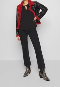 Schwarze Lederjacke mit rotem Kunstfellfutter, schwarzes Oberteil mit Schlüsselloch, schwarze ausgestellte Jeans und Ankle-Boots aus Schlangenhaut.