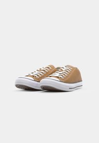 Beige canvas lage sneakers met witte veters en rubberen zool. Kenmerken zijn de gestructureerde neuskap en een dunne zwarte streep langs de middenzool.
