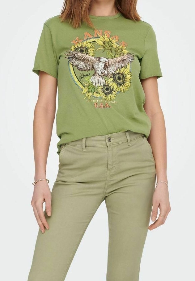 Femme portant un t-shirt vert olive avec un motif d'aigle en vol et de tournesols ainsi qu'un pantalon vert olive assorti, debout les mains détendues.