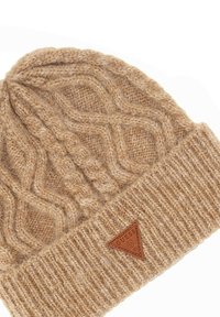 Beżowa czapka robocza z dzianiny z wzorem w warkocze, z prążkowanym mankietem i trójkątną skórzaną łatką z boku. Miękka struktura.