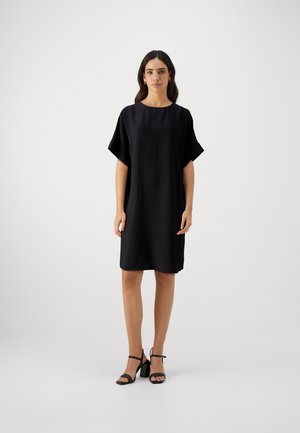 Fekete, rövid ujjú, sima anyagú shirt-dress, kerek nyakkivágással és A-vonalú szabással. Fekete csíkos magassarkúval viselve.