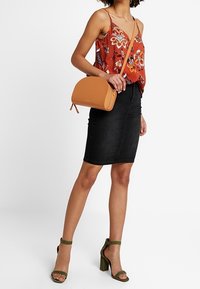 Brunaxbodyväska, blommig röd blus, svart denimkjol och gröna klacksandaler. Funktioner inkluderar justerbara axelremmar och strukturerad design.