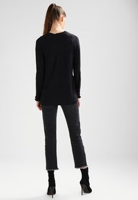 Czarny długi rękaw top z teksturowanym wzorem, połączony z ciemnoszarymi dżinsami z postrzępionymi nogawkami oraz czarnymi botkami na wysokim obcasie.