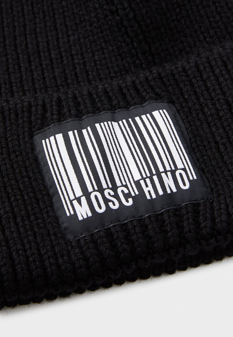 Schwarze Strickmütze mit geripptem Muster. Verfügt über ein gewebtes Etikett mit einem vertikalen Barcode und dem Wort "MOSCHINO" in Weiß.