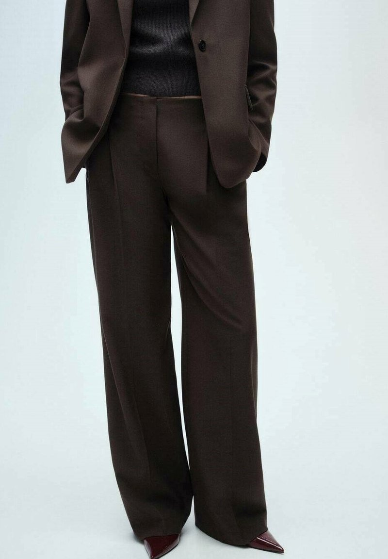 Pantalon marron sur mesure à jambes larges, confectionné dans un tissu lisse, avec une taille haute et mis en valeur par des talons aiguilles bordeaux élégants.