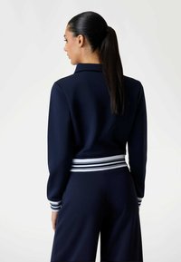Navy sweatshirt met een getailleerde pasvorm, voorzien van een witte en marineblauwe gestreepte tailleband, lange mouwen en een klassieke kraag. Gladde textuur.