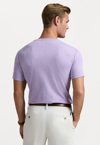 Μωβ κοντομάνικο μπλουζάκι από μαλακό ύφασμα, με στρογγυλή λαιμόκοψη και άνετη εφαρμογή, συνδυασμένο με ανοιχτόχρωμο παντελόνι.