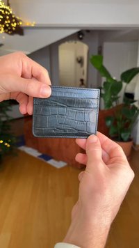 Porte-cartes en cuir bleu foncé avec un motif texturé rappelant la peau de crocodile, doté de plusieurs compartiments pour cartes et du nom de la marque embossé.