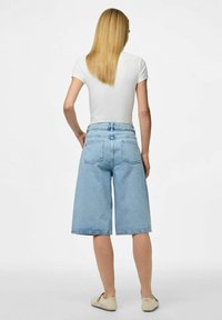 Ljust blå denim culotter med en avslappnad passform, med hög midja, bakfickor och en lätt fransad kant. Vit T-shirt och beige skor.