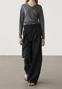 Grijze lange mouw V-hals top gecombineerd met zwarte wijde broek. De broek heeft een hoge tailleband en is gemaakt van een lichtgewicht stof.