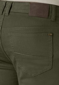 Olive green cotton-blend pants featuring a textured finish, a back patch pocket, and a brown leather brand label on the waistband.