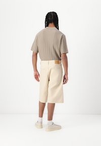 Polo de rayas en color beige con mangas cortas, combinado con pantalones cortos crema de longitud hasta la rodilla. Los zapatos son de color gris claro con suela gruesa.