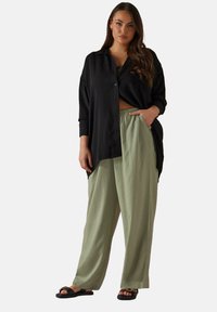 Svart oversize skjorta med knappar, ljusgröna vida byxor med resårmidja och svarta sandaler med spännen.