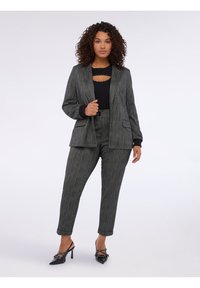 Harmaa raitapuku ja siihen sopivat housut, valmistettu teksturoidusta kankaasta. Mukana musta pusero, jossa on leikattu design, ja mustat kärkitossut korostuksilla.