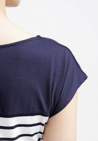 Camiseta de color azul marino con mangas cortas, que presenta rayas horizontales blancas en la mitad inferior. Material de algodón suave con un corte relajado.