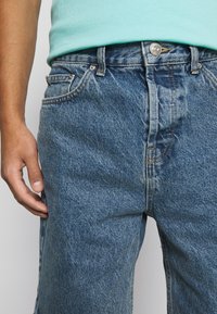 Ljusblå denimjeans med rak benprofil, klassisk femficksdesign och metallknappstängning vid midjan.