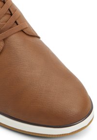 Brown textured leather sneaker with a rounded toe, lace-up design, and a white rubber sole featuring a subtle striped pattern.
