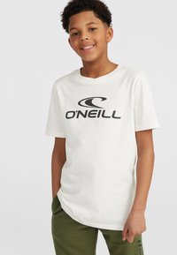 Camiseta de algodón blanca con un gran logo negro de "O'Neill". Manga corta y escote redondo. Combinada con pantalones verdes.
