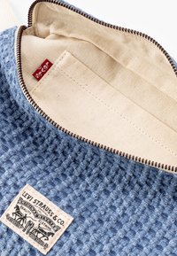 Pochette in tessuto blu intrecciato con fodera interna in cotone, cerniera marrone e etichetta bianca Levi Strauss & Co. con branding dettagliato.