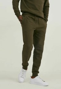 Dunkelgrüne Sweatpants aus weichem Material, mit elastischem Bund und Kordelzug sowie Seitentaschen; kombiniert mit weißen Sneakern.