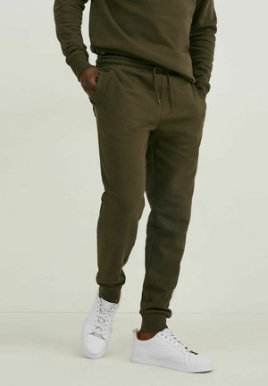 Mørkegrønne sweats, lavet af blødt materiale, med elastisk talje og snøre samt sidelommer; sat sammen med hvide sneakers.