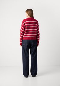 Rood en roze gestreepte gebreide trui met een cropped ontwerp en geribbelde zoom, gecombineerd met loszittende donkere spijkerbroeken.