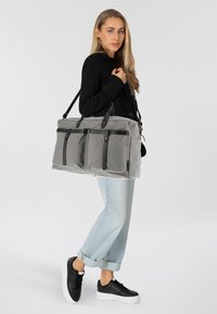 Sac en tissu gris et durable avec des accents en cuir noir et trois poches extérieures. Forme rectangulaire et sangle ajustable pour un transport polyvalent.
