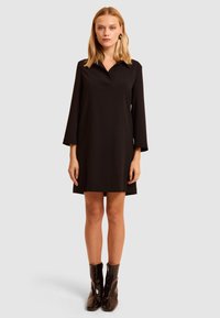 Czarna sukienka z kołnierzykiem, długimi rękawami, lekko dopasowanym krojem i gładką fakturą, zestawiona z połyskującymi czarnymi botkami za kostkę. Minimalistyczny design.