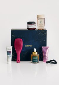 En blå låda med guldprickar innehåller sex hårvårdsprodukter: en rosa hårborste, krämer och oljor i olika behållare och tuber.