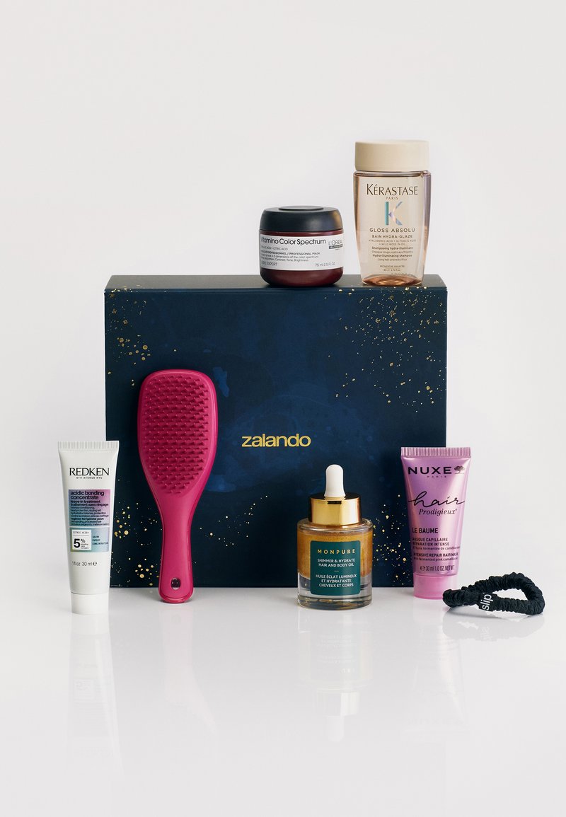 En blå låda med guldprickar innehåller sex hårvårdsprodukter: en rosa hårborste, krämer och oljor i olika behållare och tuber.