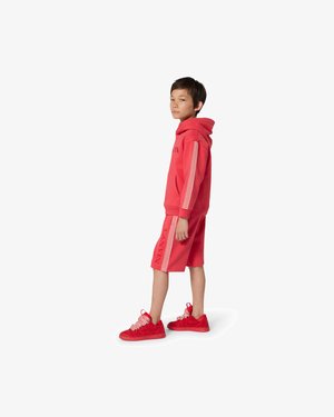 Red hoodie with logo, matching red shorts, and red sneakers. Features textured accents and patterned side stripe on both the hoodie and shorts.