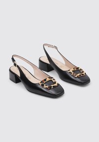 Zapatos negros de piel con tirantes al tobillo, punta cuadrada, tacón bajo y un acento de hebilla con estampado de leopardo en el frontal. Textura suave.