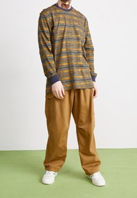 Mörkgrå långärmad t-shirt med orange horisontella ränder, med rund halsringning. Kombinerad med lösa bruna byxor och vita sneakers.