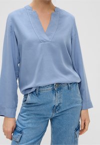 Maglietta azzurro chiaro a maniche lunghe con scollatura a V e dettagli cuciti, abbinata a jeans in denim chiaro con tasche laterali e una vestibilità rilassata.