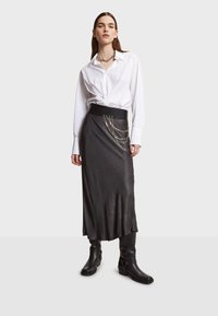 Jupe en satin noire avec une taille ajustée et des accentuations en chaîne argentée, associée à une chemise blanche à boutons et des bottes noires jusqu'au genou.