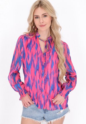 Blusa rosa e blu con stampa, colletto con laccetto, chiusura con bottoni, maniche lunghe con polsini a volant e tessuto leggero e trasparente.