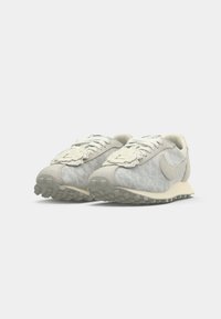 Par tenisica u svijetlo sivoj i boji off-white marke Nike s vezicama i teksturiranim potplatima, blago okrenutih udesno.