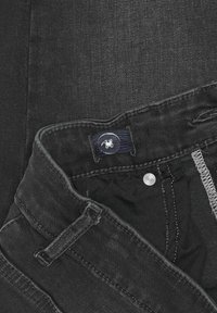 Svarta denimjeans med knäppning, övre knappen har en logotyp och synliga söm detaljer. Tyget verkar stabilt och texturerat.