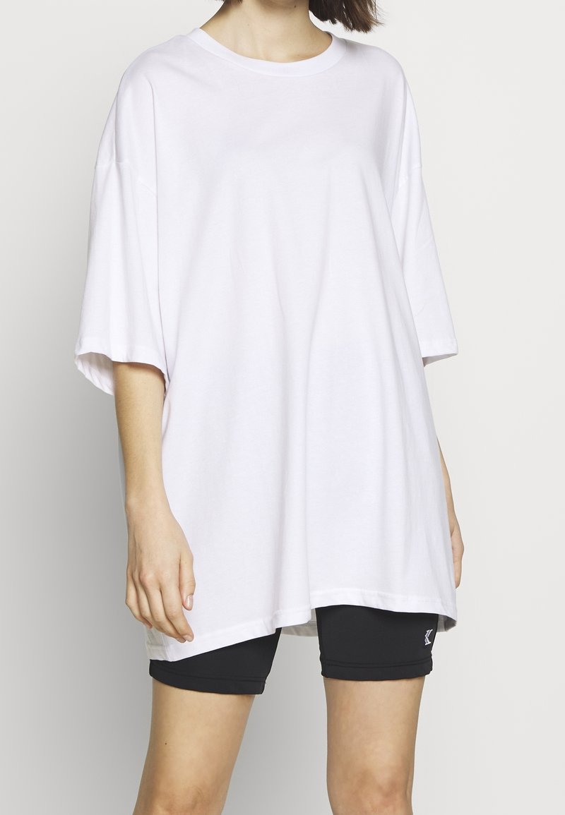 White oversized t-shirt made from soft cotton, featuring a round neck and short sleeves. Worn over black athletic shorts.