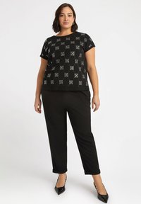 Top negro de manga corta con un patrón geométrico blanco, combinado con pantalones negros ajustados. El conjunto presenta un corte relajado y una textura suave.