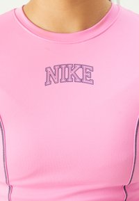 Różowa koszulka sportowa z elastycznego materiału, z okrągłym dekoltem i logo "Nike" w ciemnofioletowym kolorze na piersi.