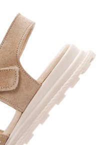 Sandal in suede beige con una larga fascia, chiusura in velcro e suola in gomma bianca spessa con dettagli testurizzati.