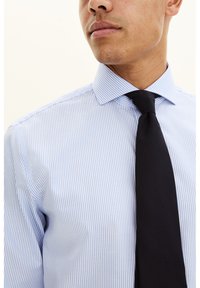 Vaaleansininen raidallinen paita, jossa on siisti kaulus, yhdistetty yksiväriseen mustaan kravattiin. Sileä kangaspinta ja istuva malli.