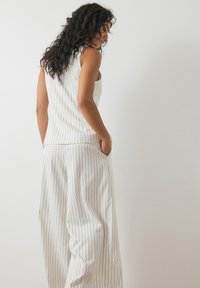 White pinstripe sleeveless top and wide-legged pants, featuring a smooth texture and side pockets for practicality.
